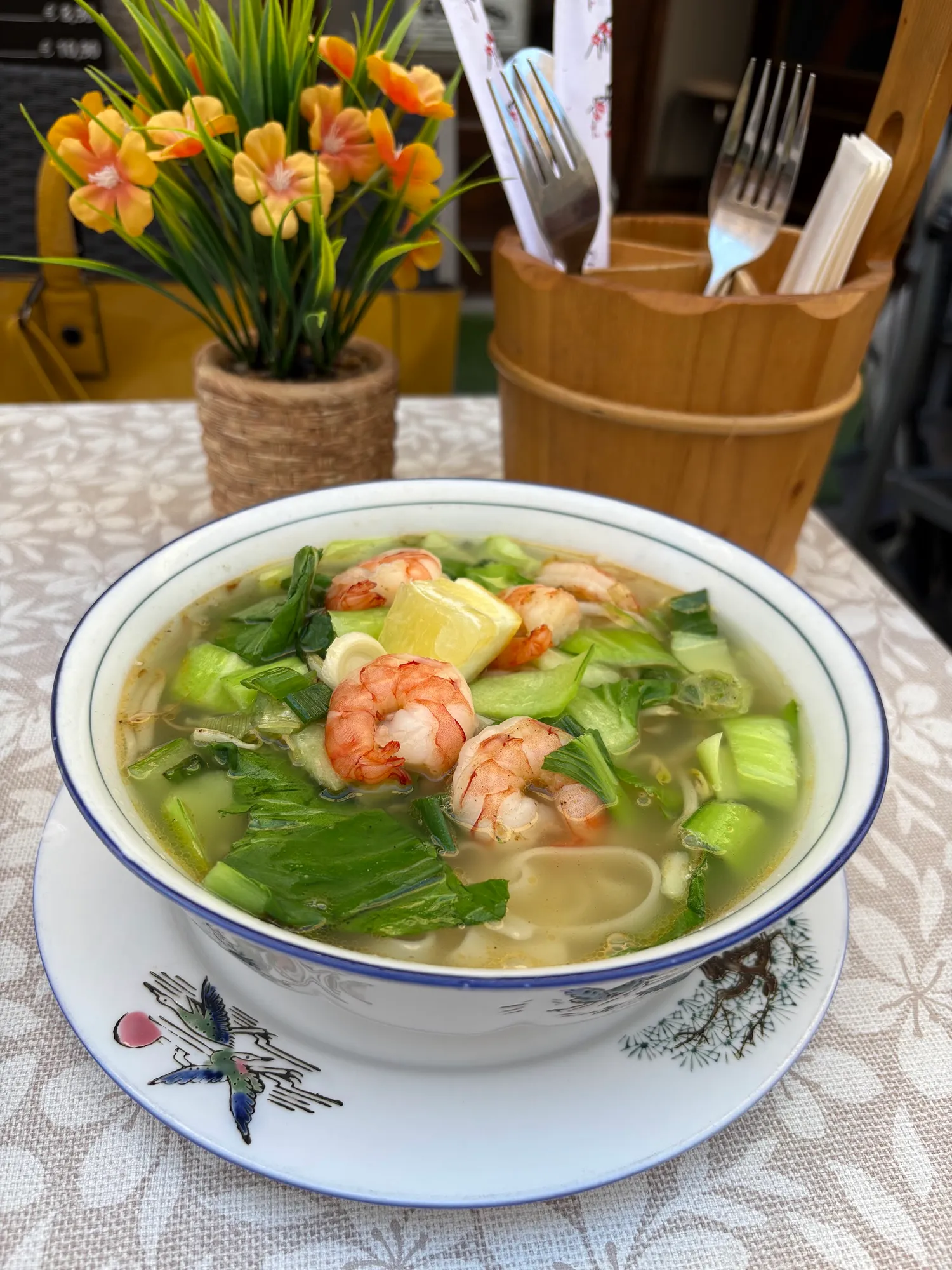 Nudelsuppe mit Garnelen, Pak Choi und Zitrone in einer weißen Porzellanschale mit blauem Rand und Vogelmotiv