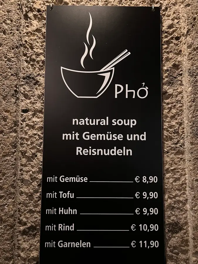 Schwarzes Schild an der Steinmauer: Phở, natural soup mit Gemüse und Reisnudeln